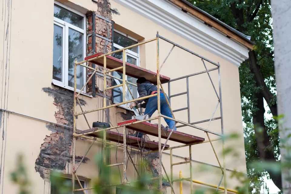 Man on a scaffold repairs a stucco wall.